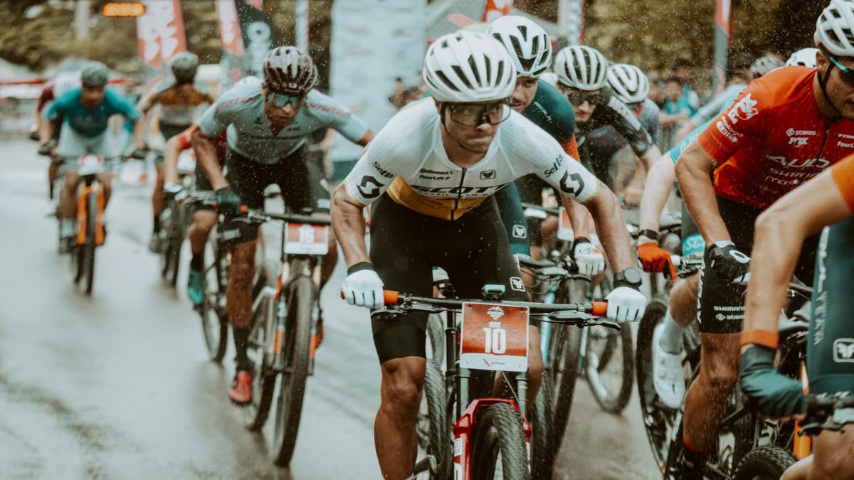 Cyclists in a competitive road race pedaling hard under rainy conditions.